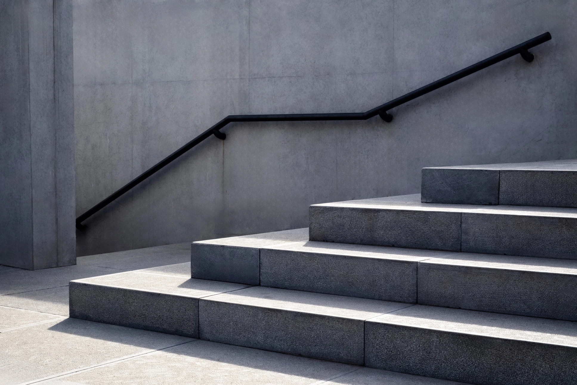 Escalier extérieur en béton gris avec marches géométriques et main courante noire métallique