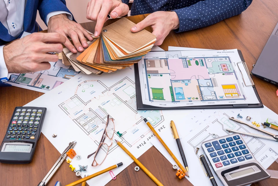 R&eacute;union de travail autour d'une table en bois avec deux personnes consultant des nuanciers de mat&eacute;riaux et plans d'architecture